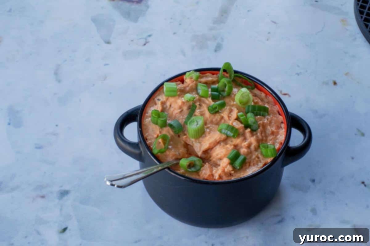 Finished Weight Watchers Buffalo Chicken Dip in a black bowl with a serving spoon, garnished with fresh green onions.