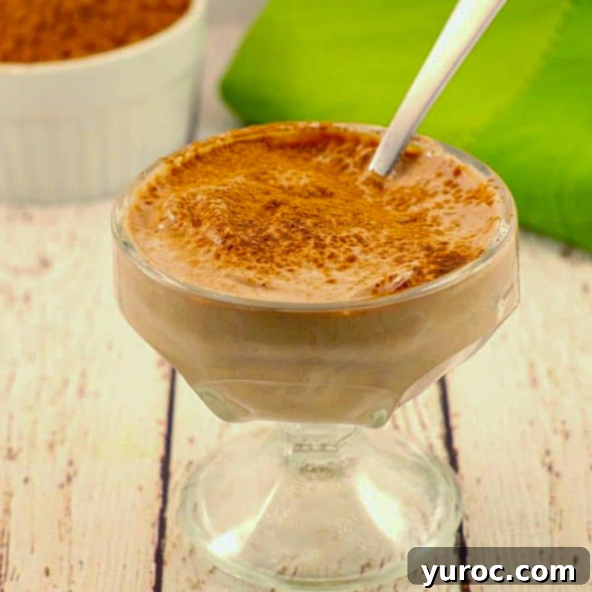 Rich chocolate Greek yogurt in a clear glass dessert dish, garnished with a spoon, highlighting its creamy texture.