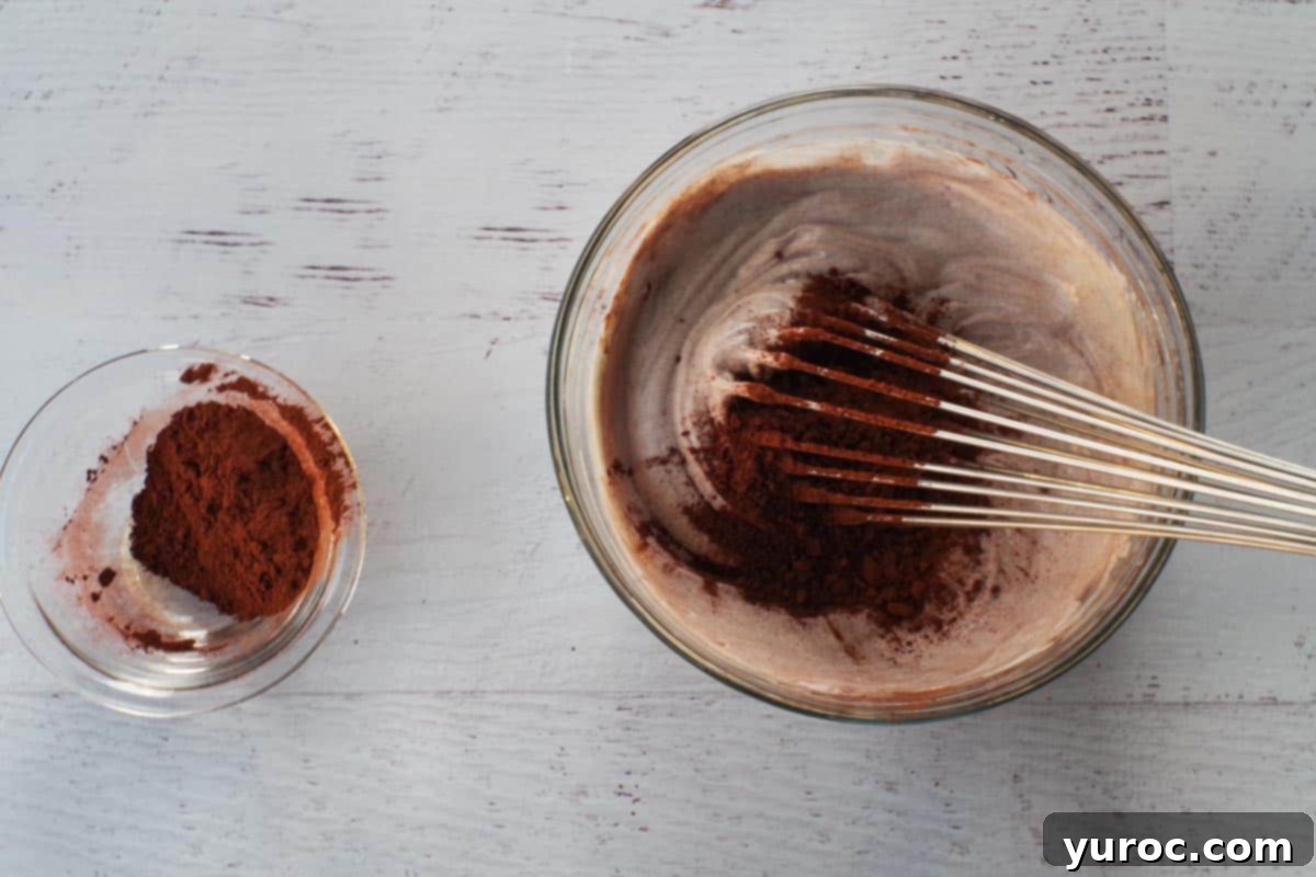 A whisk gently incorporating unsweetened cocoa powder into the Greek yogurt and agave mixture, preventing lumps.