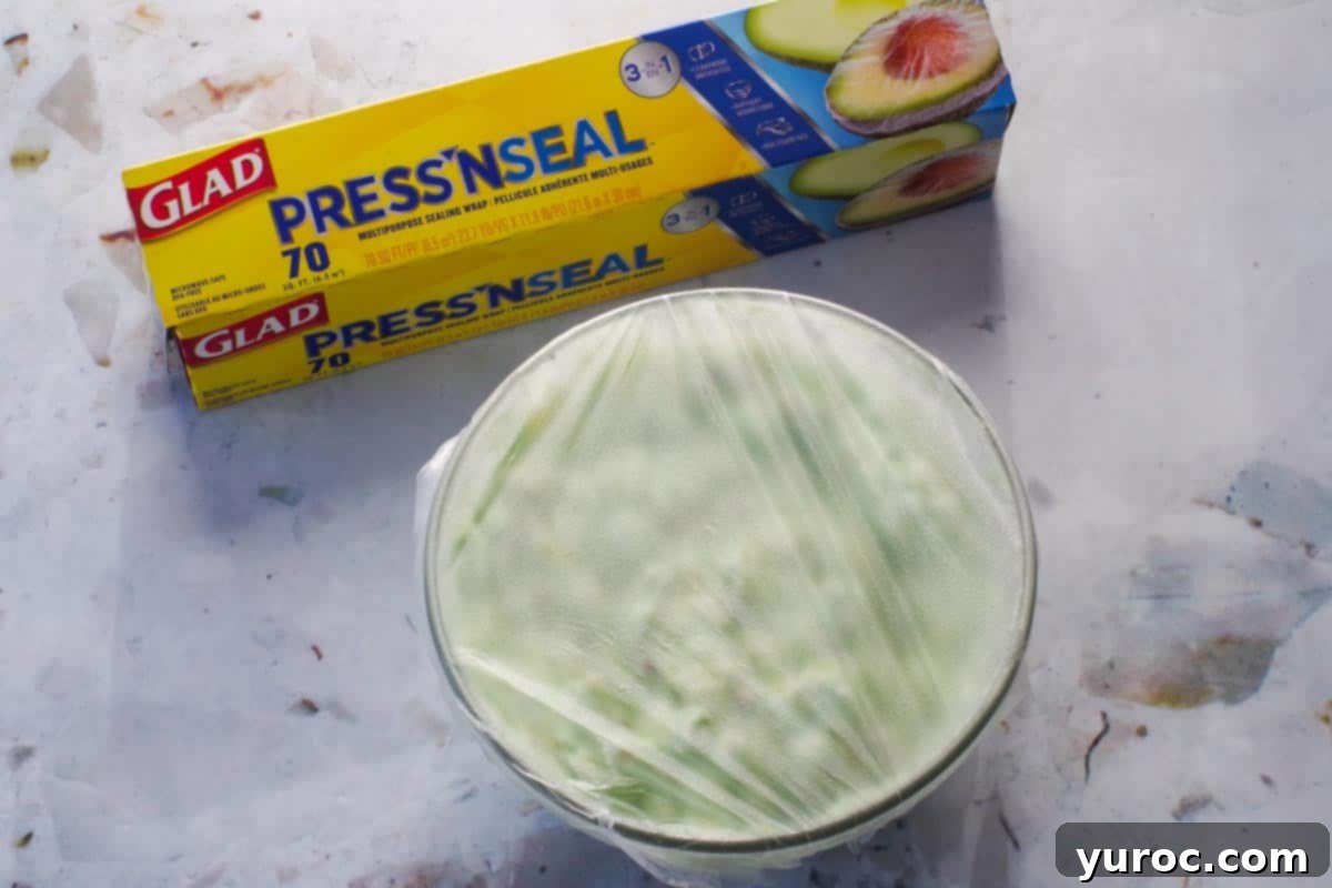 Creamy Pistachio Fluff 9 Pistachio salad in a glass bowl covered with plastic wrap, with a package of Glad Press 'n Seal behind it, indicating it's ready for refrigeration.