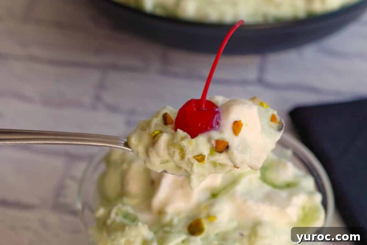 Creamy Pistachio Fluff 10 A serving spoon lifting a spoonful of fluffy green Pistachio Fluff out of a dessert bowl, with more of the dessert visible in the bowl.