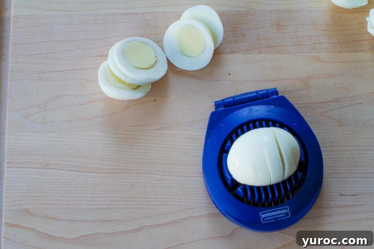 Egg being sliced with an egg slicer and more sliced eggs behind it on the cutting board.