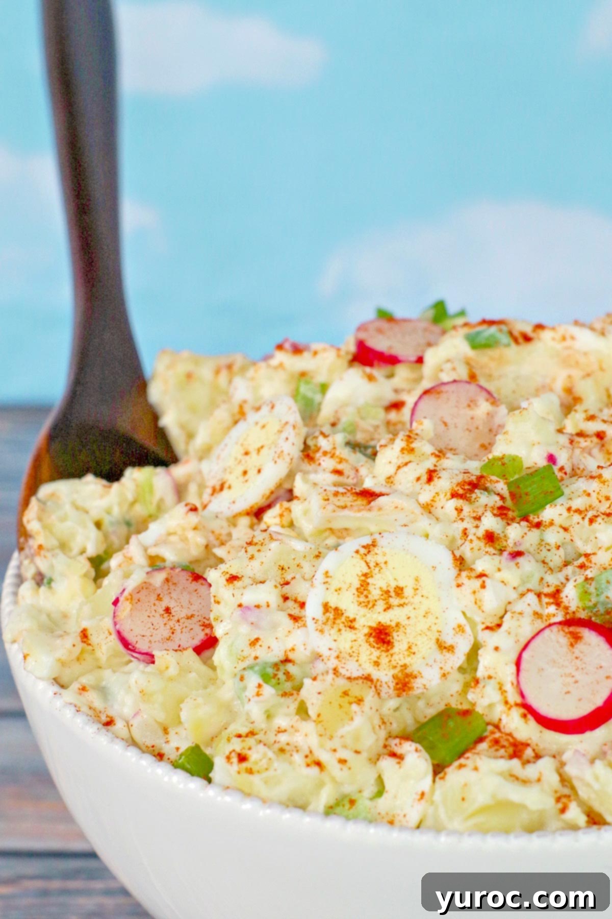 Potato salad in white bowl with brown serving spoon