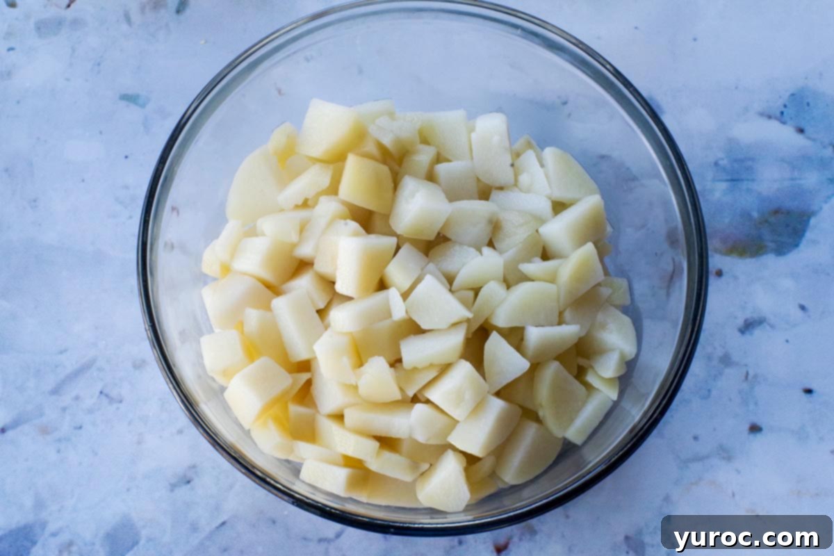 Potatoes cooked, drained and chilled in a large glass bowl.