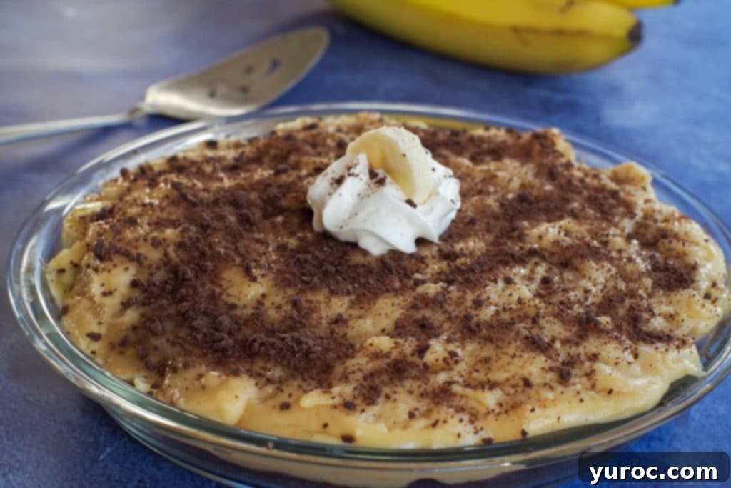 Lightened Up Old Fashioned Banana Cream Pie 2 A whole healthy banana cream pie sits on a blue surface, with a pie server in the background, ready to be served.