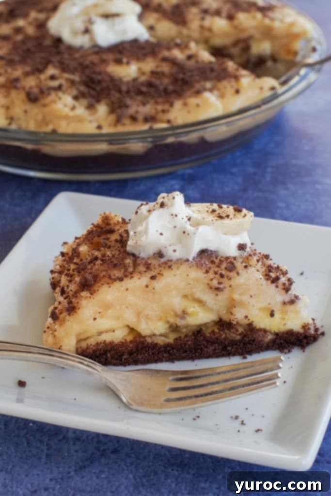 Lightened Up Old Fashioned Banana Cream Pie 5 Another enticing shot of a slice of healthy banana cream pie on a white plate, with a whole pie in the background, showcasing its creamy layers and graham cracker crust.