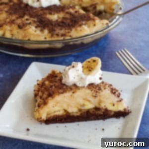 Lightened Up Old Fashioned Banana Cream Pie 6 A slice of healthy banana cream pie on a white plate with a whole pie in the background.