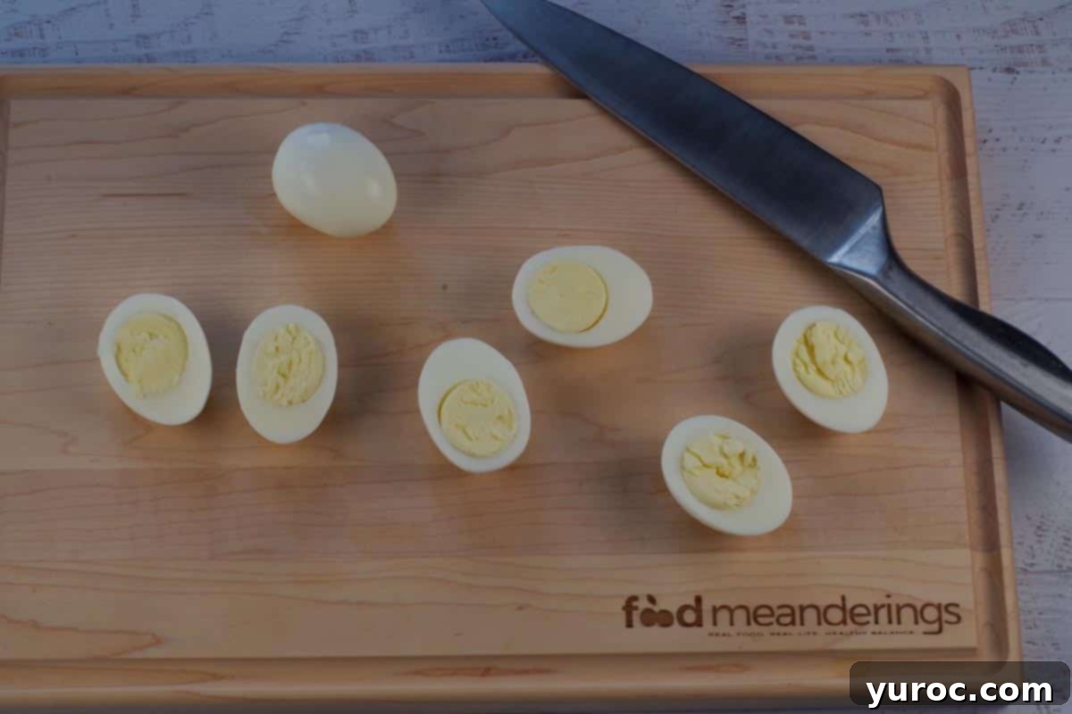 4 eggs on a cutting board with a sharp knife. 3 of the 4 eggs are cut in half lengthwise.