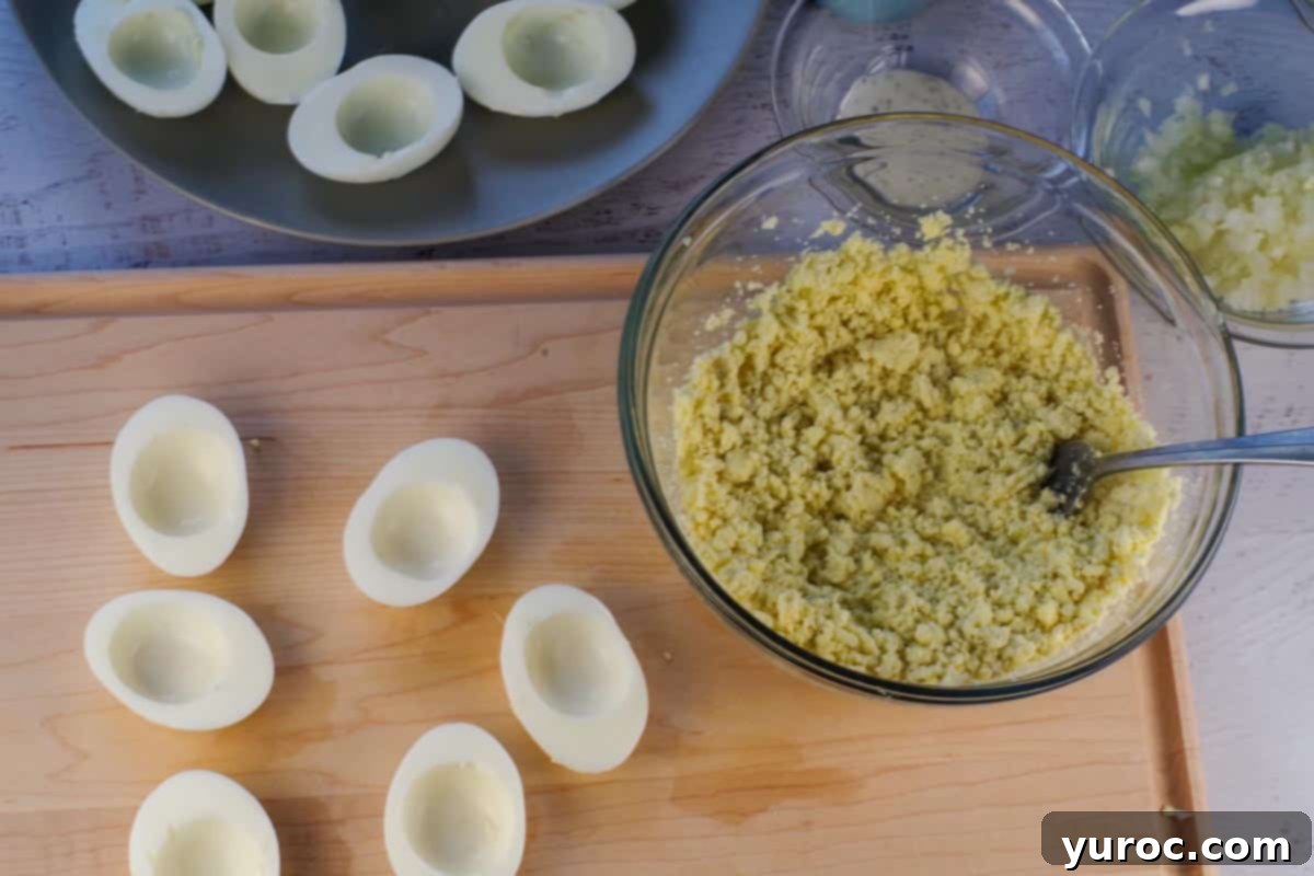Egg yolks removed from eggs and mashed in a glass bowl with a fork and egg whites beside it on the cutting board.