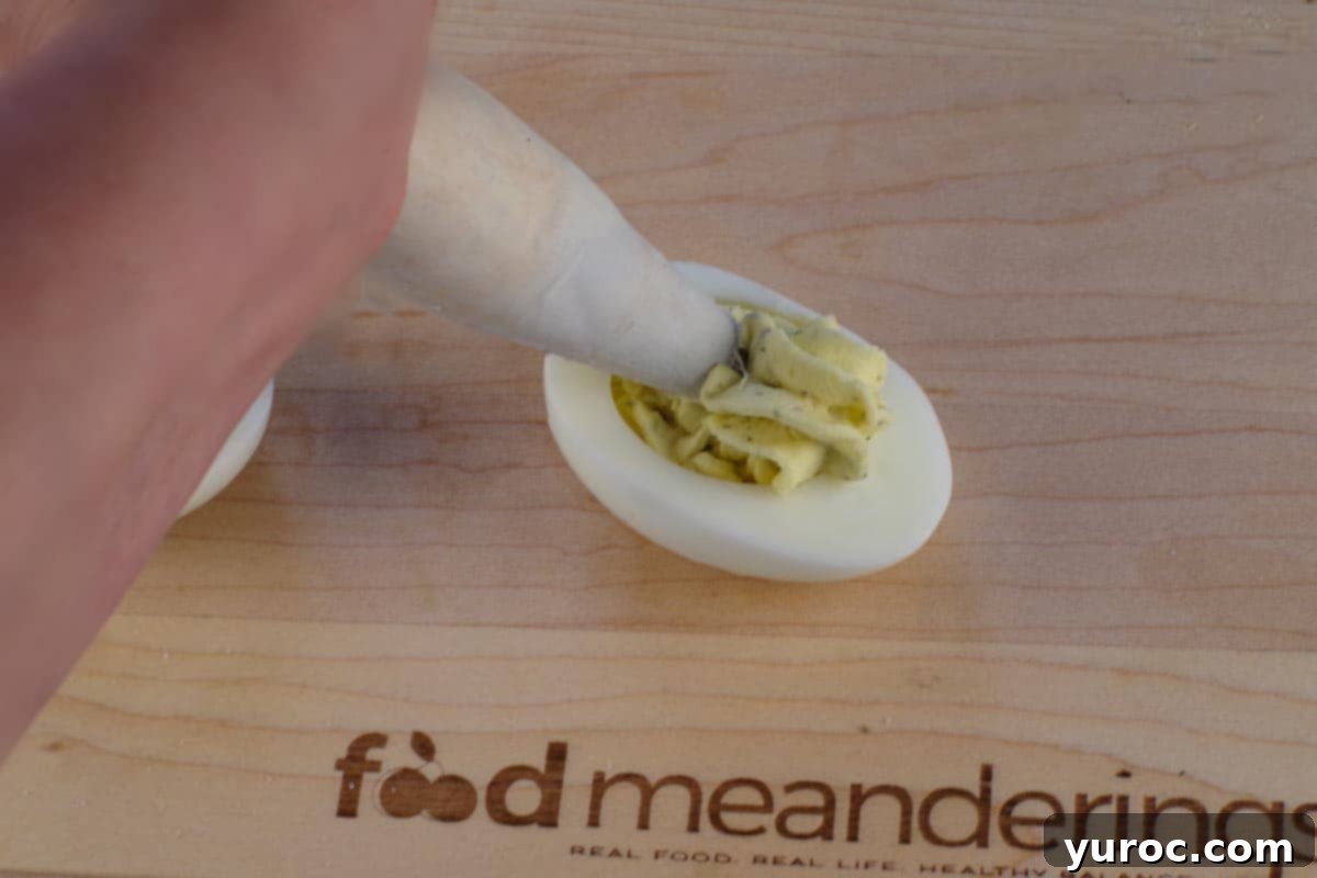 Egg yolk filling being piped into egg white with 1M tip in pastry bag, on a cutting board.