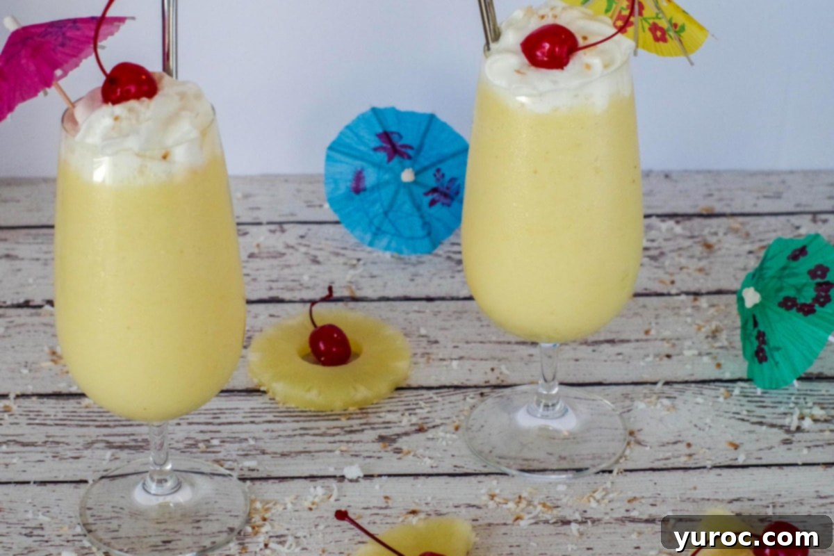 Two healthy Pina Colada drinks on a white faux wood surface, garnished with pineapple, maraschino cherries, and small umbrellas.
