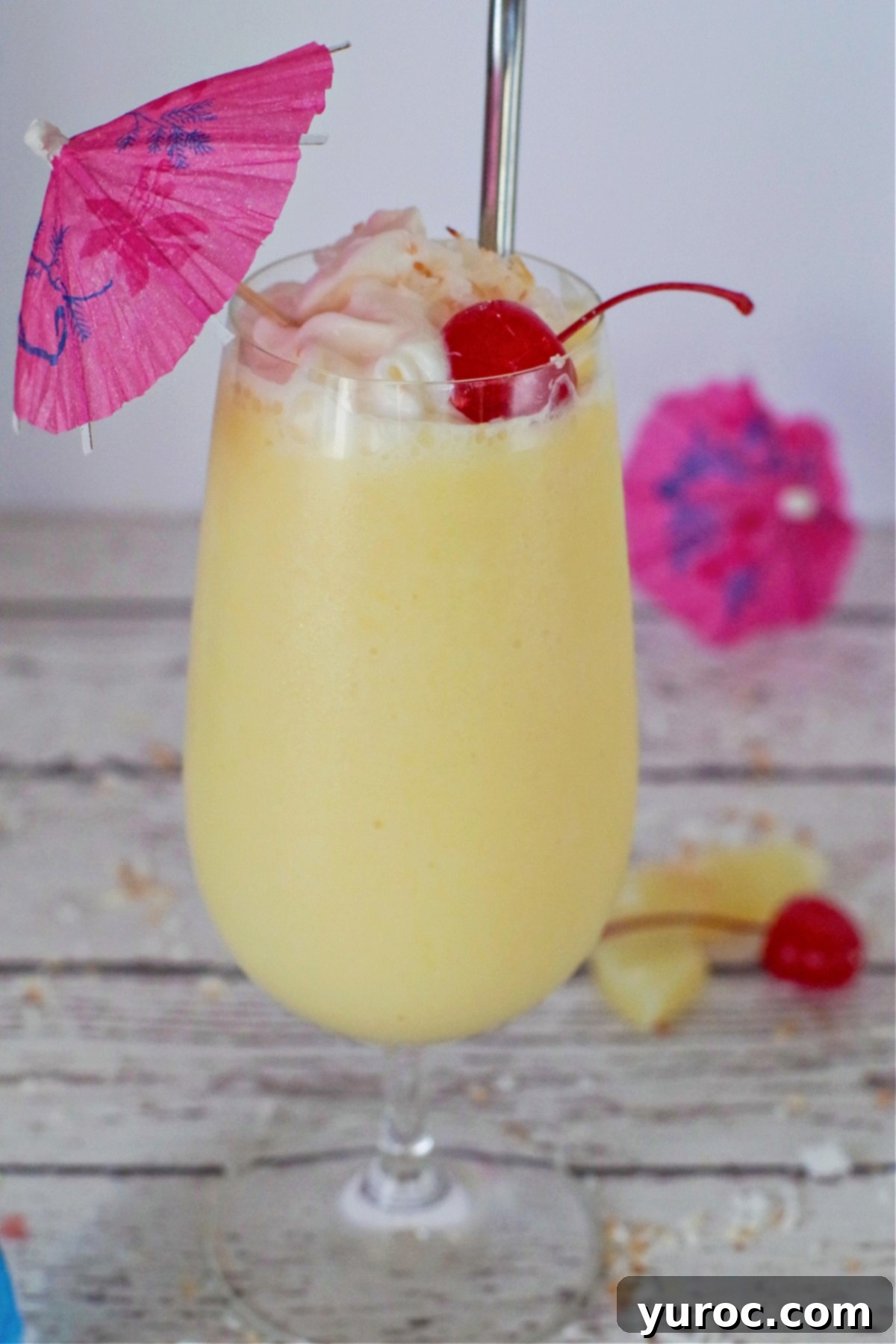 A single healthy Pina Colada drink on a white faux wood surface, garnished with pineapple, maraschino cherry, and a cocktail umbrella.