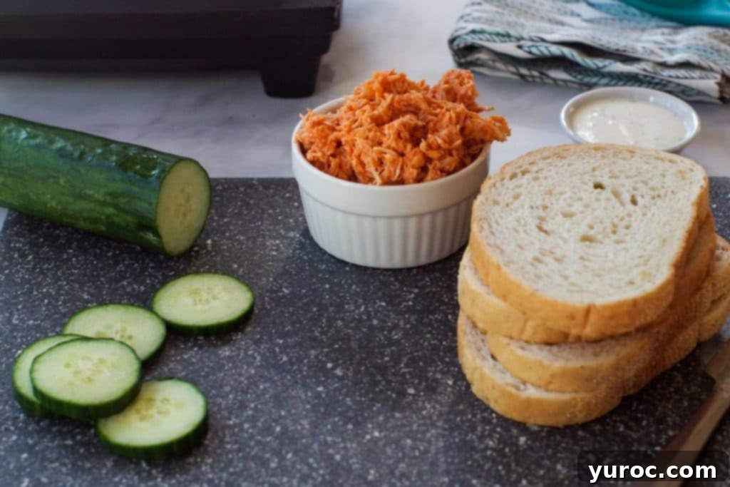 ingredients for buffalo chicken panini- bread, cucumbers, ranch dip and buffalo chicken on cutting board