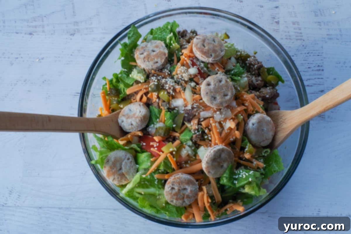 Big Mac salad in large glass bowl with wooden salad servers in bowl.