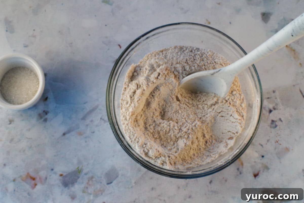 Dry ingredients mixed together in medium glass bowl with marble silicone spoon.