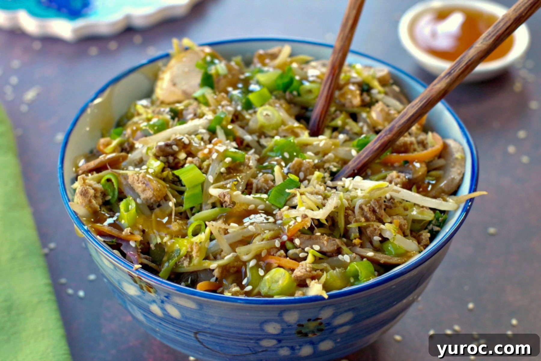 Egg roll in a blue flowered bowl with chopsticks and a small white dish of plum sauce in the background