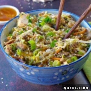 Egg roll in a blue flowered bowl with chopsticks and a small white dish of plum sauce in the background and wok with more egg roll in a bowl in the background