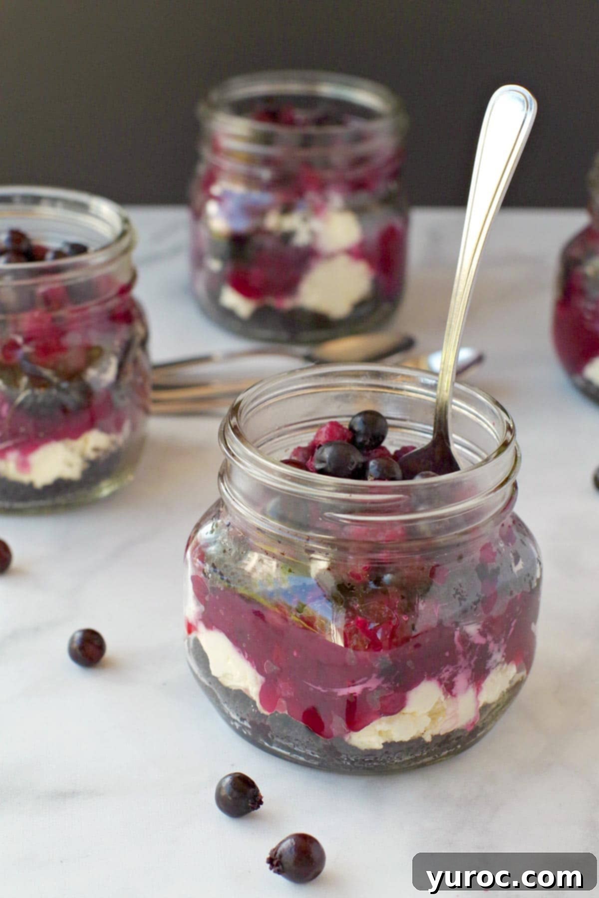 No-Bake Saskatoon Berry Cheesecake Jars 12 4 jars of No Bake Saskatoon berry cheesecake (one in front with spoon)
