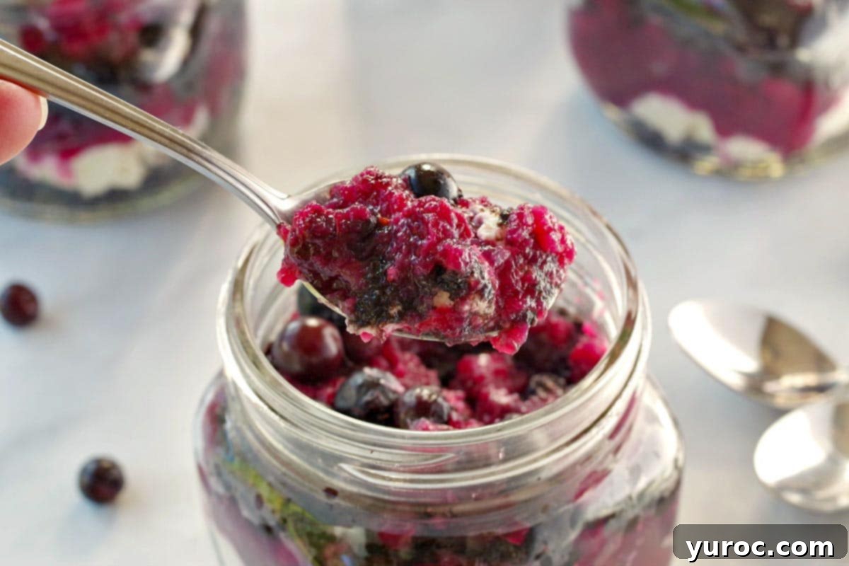 No-Bake Saskatoon Berry Cheesecake Jars 3 saskatoon berry cheesecake being lifted out of jar with a spoon