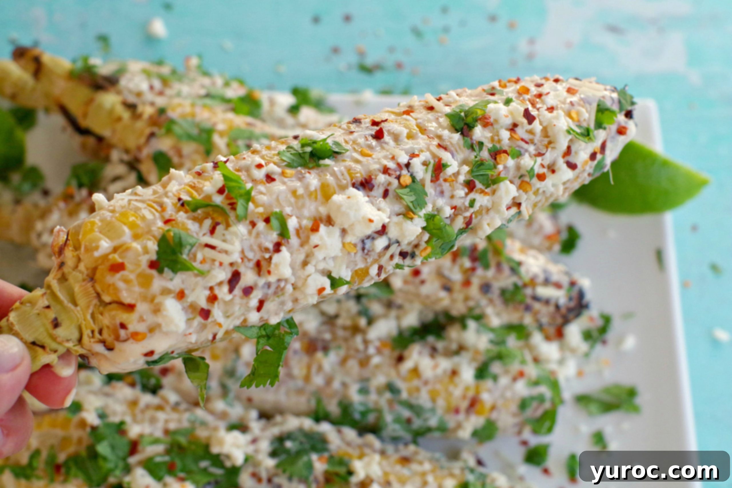 mexican corn on the cob being held up over platter