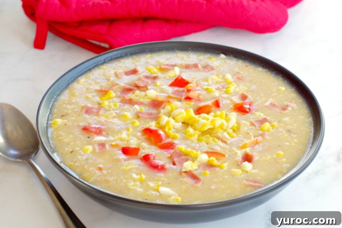 Wholesome Velvety Sweet Corn Chowder 2 A bowl of healthy creamy corn chowder with turkey bacon, garnished with fresh herbs, against a soft-focus background of red oven mitts.