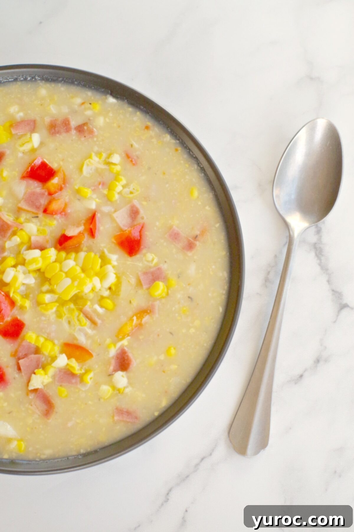 Wholesome Velvety Sweet Corn Chowder 11 A beautifully presented bowl of creamy corn chowder, garnished and ready to eat, with a spoon resting in it.