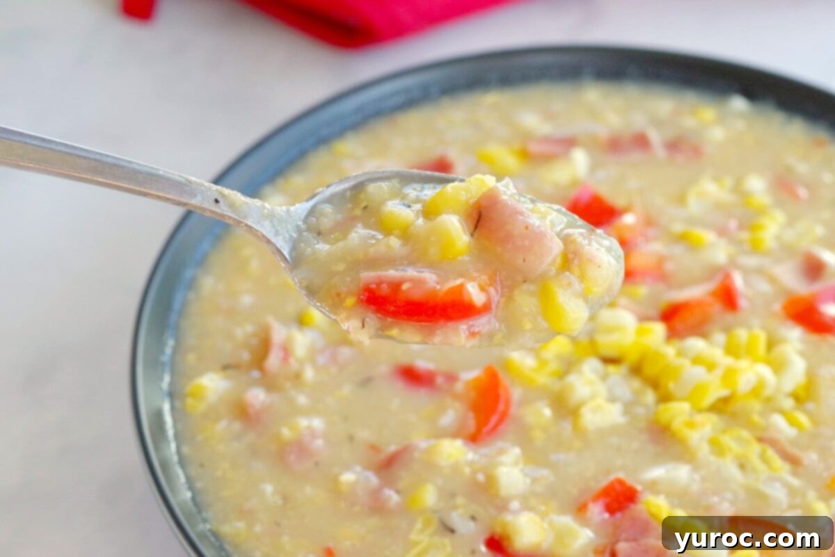 Wholesome Velvety Sweet Corn Chowder 5 A spoon lifting a creamy portion of corn chowder with visible corn kernels and bits of turkey bacon from a black bowl, highlighting the soup's rich texture.