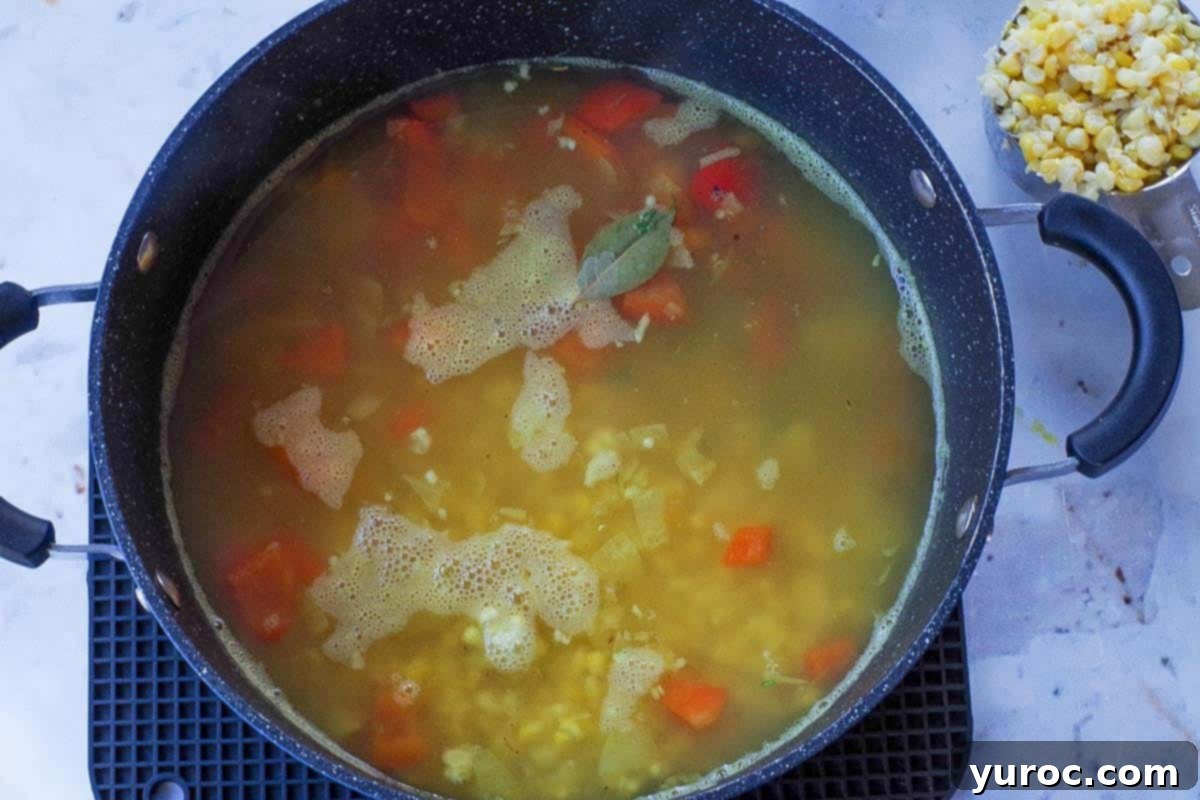 Wholesome Velvety Sweet Corn Chowder 8 A large pot filled with a simmering corn chowder base, featuring diced potatoes, some corn kernels, fresh thyme, and a bay leaf, seasoned with salt and pepper.