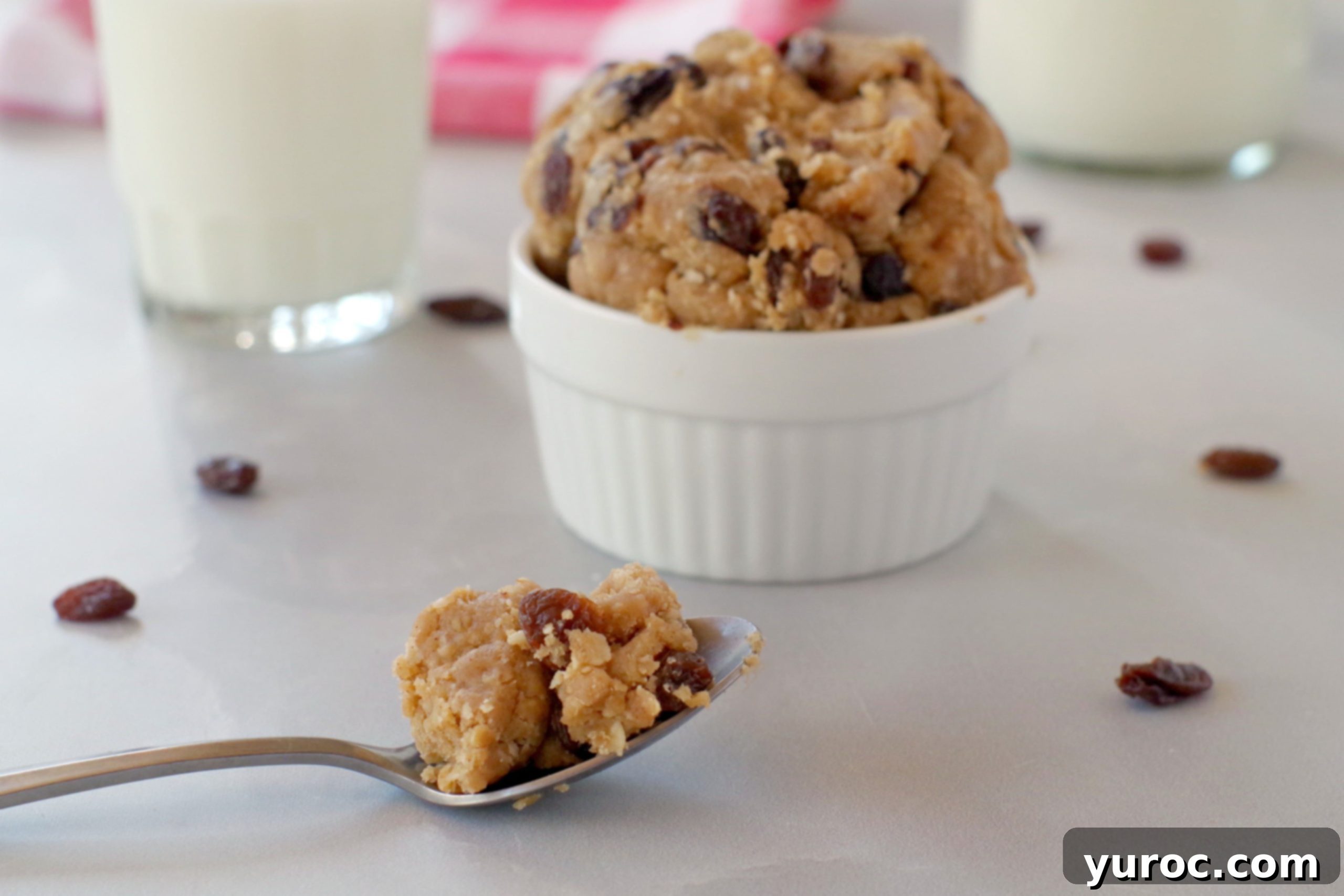 Oatmeal Raisin Dough Delight 3 A spoonful of homemade edible cookie dough held above a white bowl filled with more dough, showcasing its rich texture.