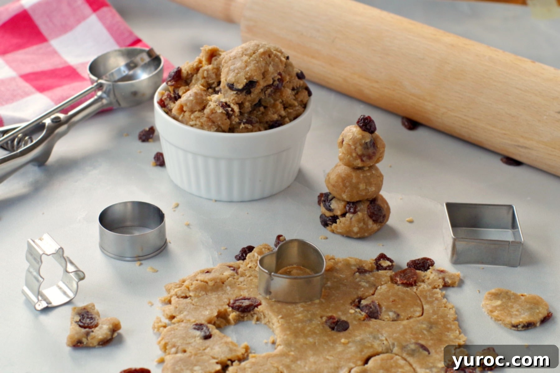 Oatmeal Raisin Dough Delight 4 Edible cookie dough rolled flat and cut into various shapes using cookie cutters, with a rolling pin in the background.