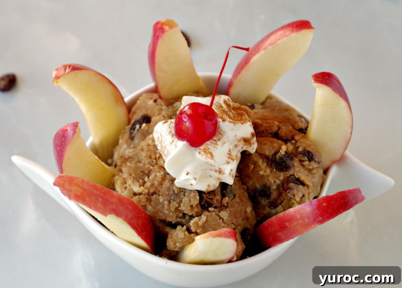 Oatmeal Raisin Dough Delight 6 A white bowl of edible cookie dough dip surrounded by perfectly sliced apple pieces.