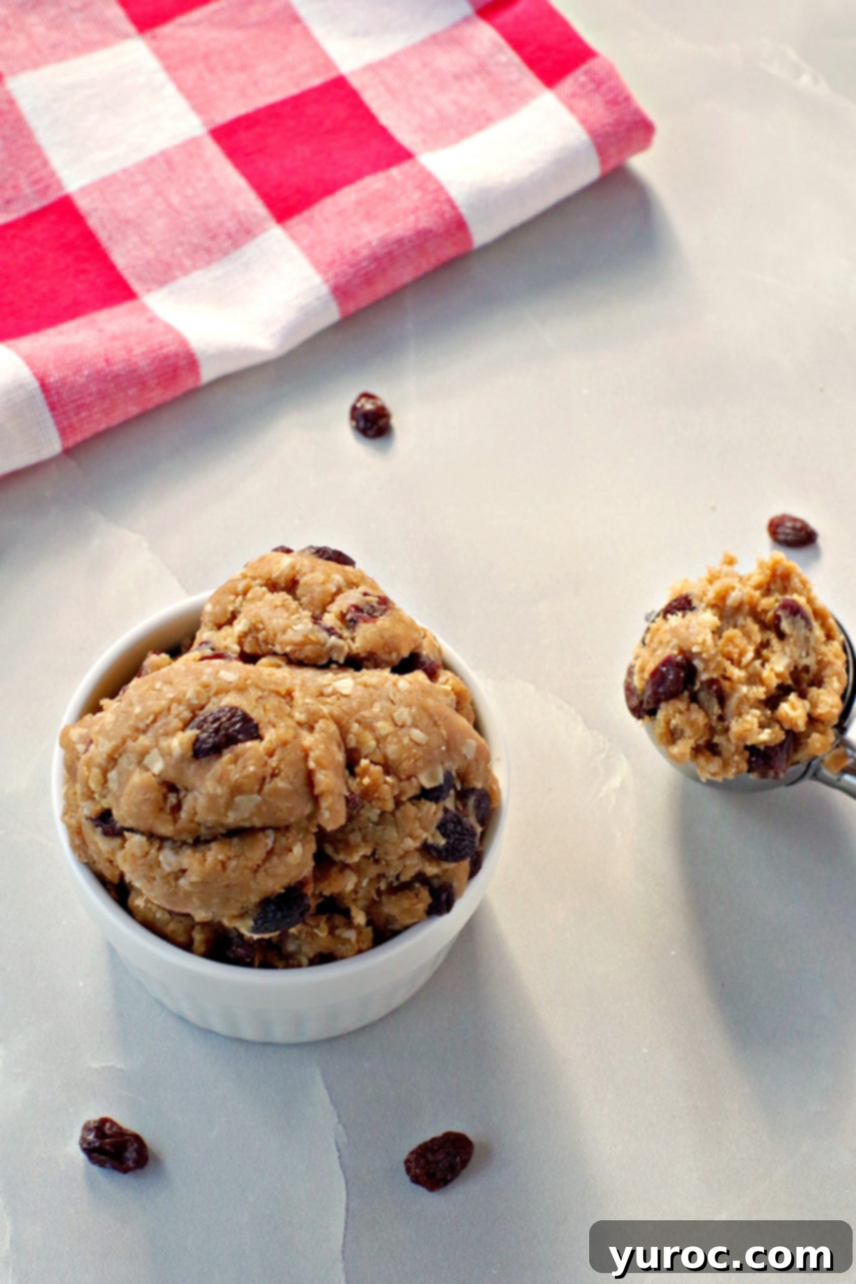 Oatmeal Raisin Dough Delight 8 A white bowl overflowing with edible cookie dough, with a cookie scoop resting beside it, ready for serving.