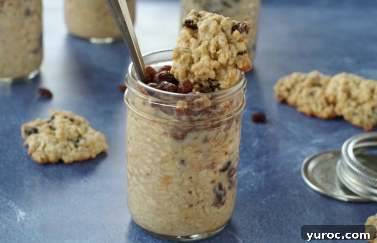 Oatmeal Raisin Cookie Dough Overnight Oats 9 A jar of oatmeal raisin cookie overnight oats topped with a mini cookie, set against a blue background with scattered oatmeal raisin cookies.