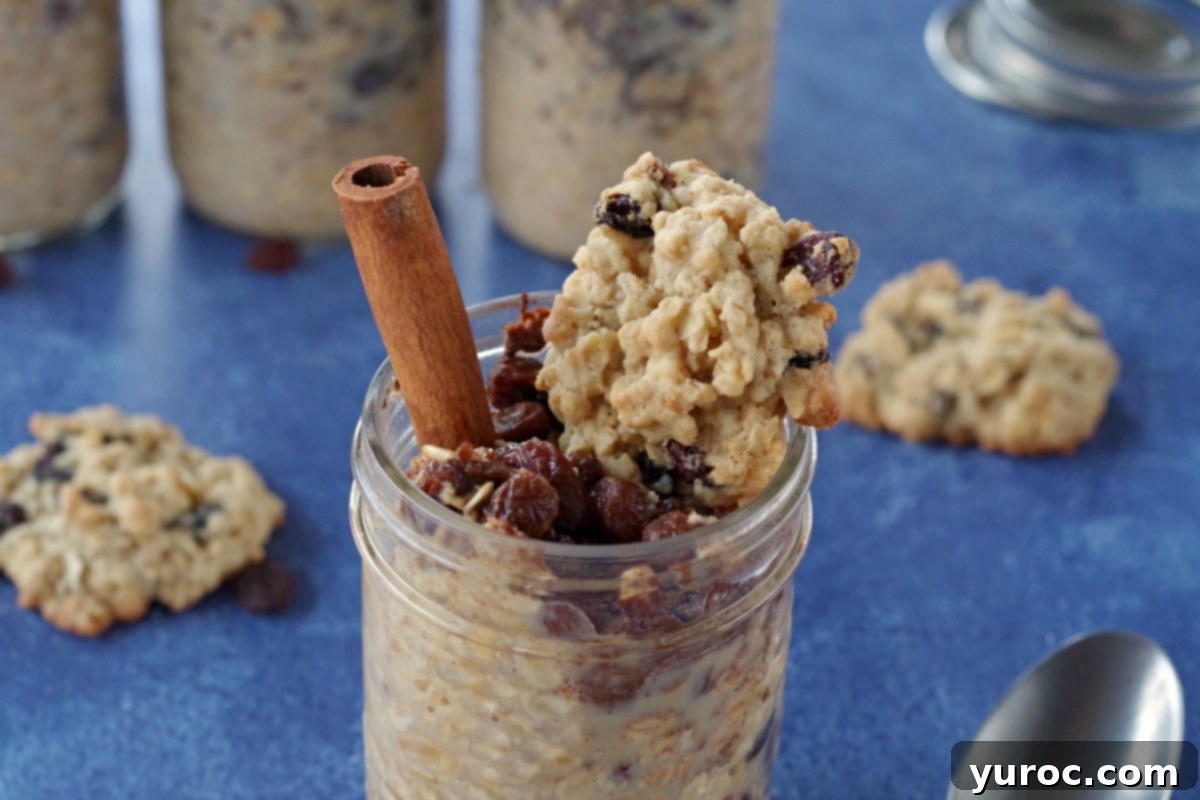 Multiple jars of oatmeal raisin cookie overnight oats on a blue background, with fresh oatmeal raisin cookies and a separate jar of oats, raisins, brown sugar, and chia seeds.