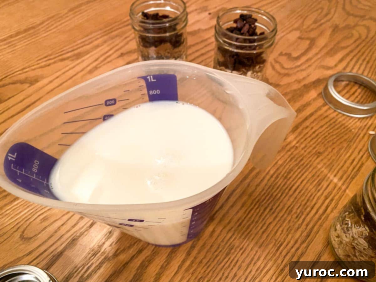 A measuring cup filled with milk, vanilla extract, and butter extract, ready to be poured into the prepared oat jars in the background.