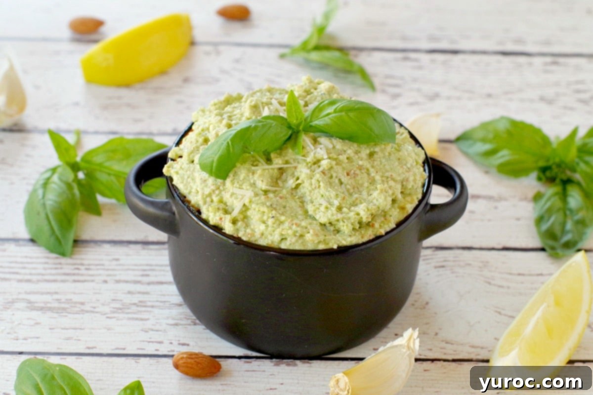 basil pesto with almond in a black dish with almonds, basil, garlic and lemon surrounding the dish