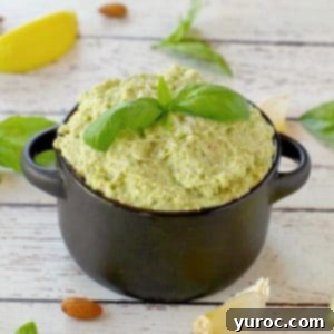 basil pesto with almond in a black dish with almonds, basil, garlic and lemon surrounding the dish