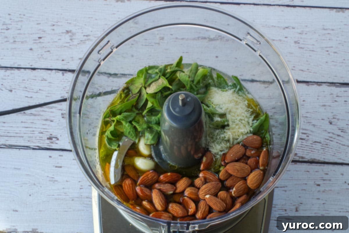 All ingredients for almond basil pesto in the bowl of a food processor.