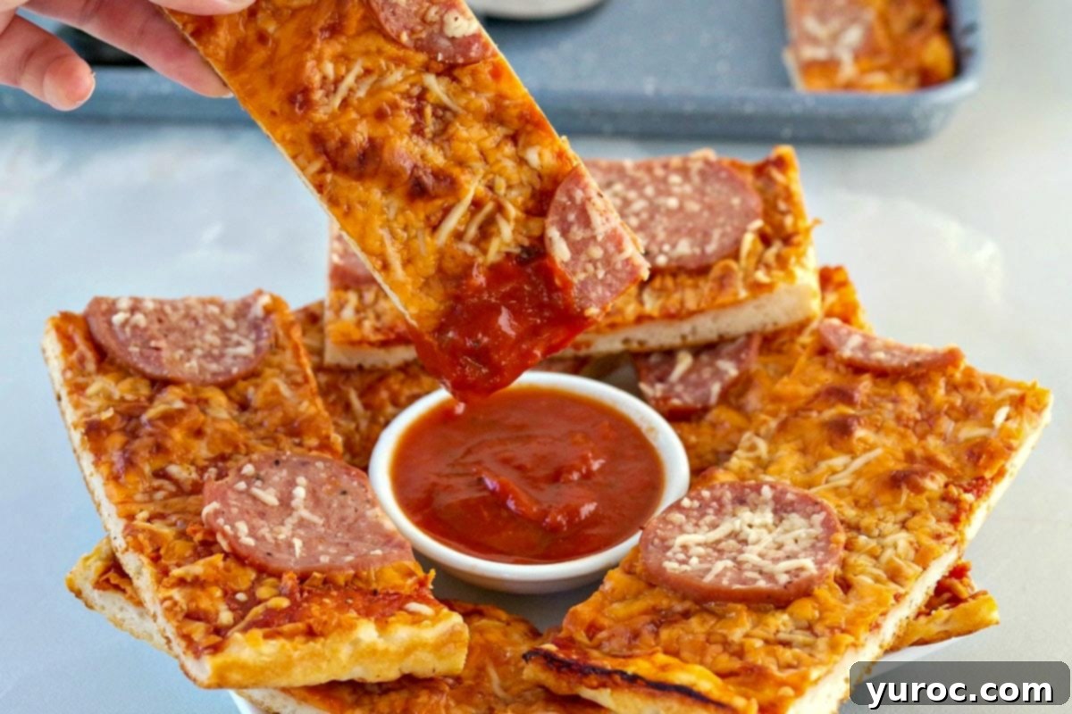 Pizza dipper being dipped into pizza sauce with pieces of pieces around it on white plate. White ranch dip on plate as well.