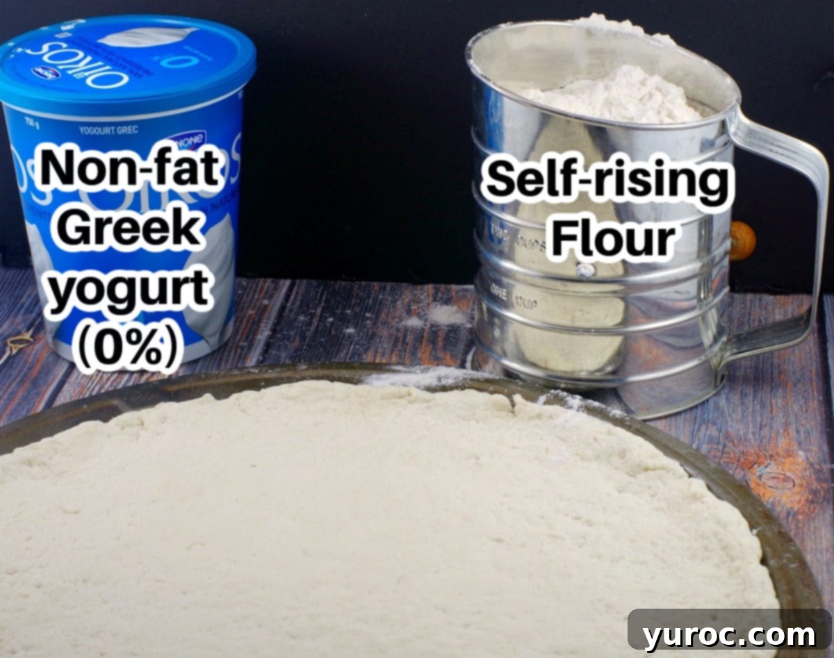 A container of non-fat Greek yogurt and a sifter with self-rise flour  (labelled) in front of 2 ingredient pizza dough on a pan