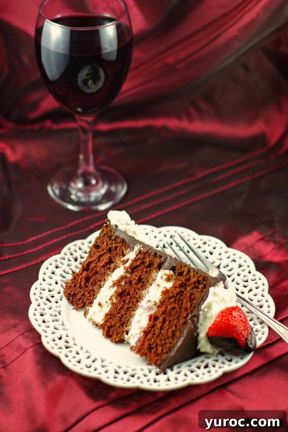 A perfectly sliced piece of Red Wine Chocolate Strawberry cake on a white plate, revealing its layers, with a glass of red wine in the background, ready for a special occasion.