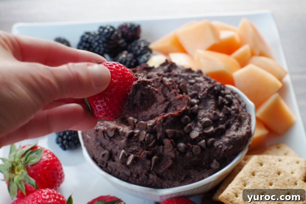 15 No-Prep Healthy School Lunches for Teens 18 dark chocolate hummus in a white petal bowl (on a white platter with fruit and crackers), with a strawberry being dipped into it