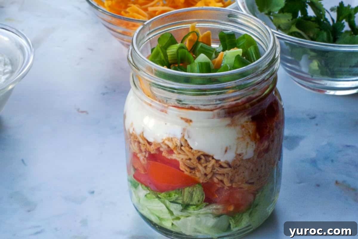 Green onions added on top of the cheese in mason jar healthy chicken taco salad.