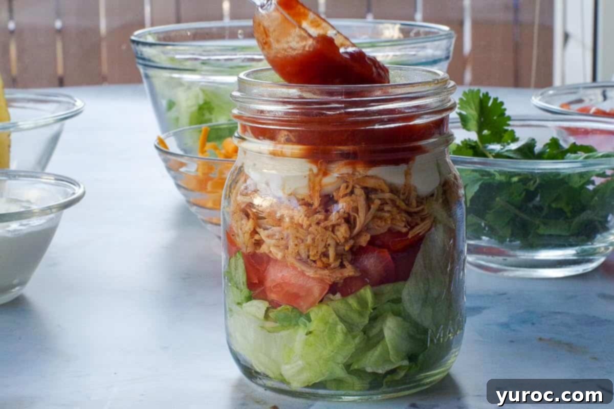 Sour cream and salsa being added to healthy chicken taco salad in a jar. 