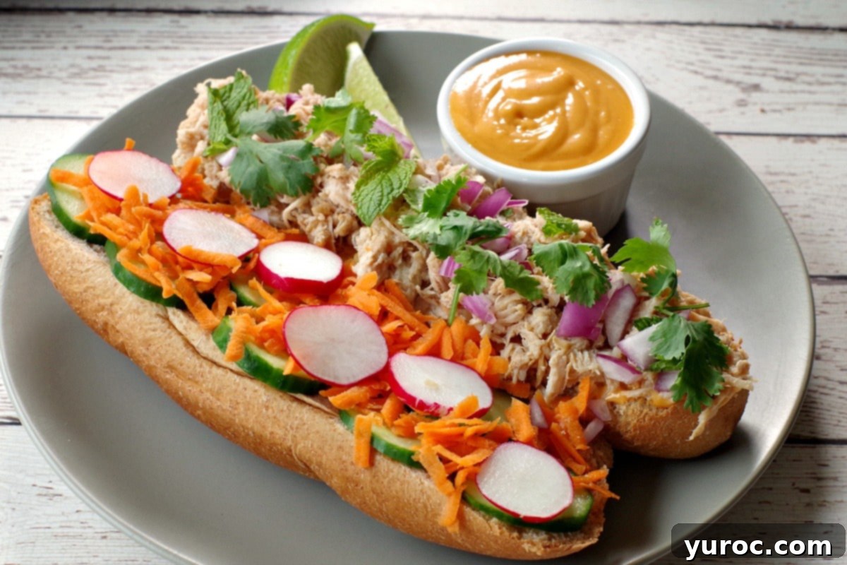 Open Slow Cooker Chicken Banh Mi Vietnamese Sub on a greenish-grey plate with lime garnish and a small white dish of Sriracha mayonnaise