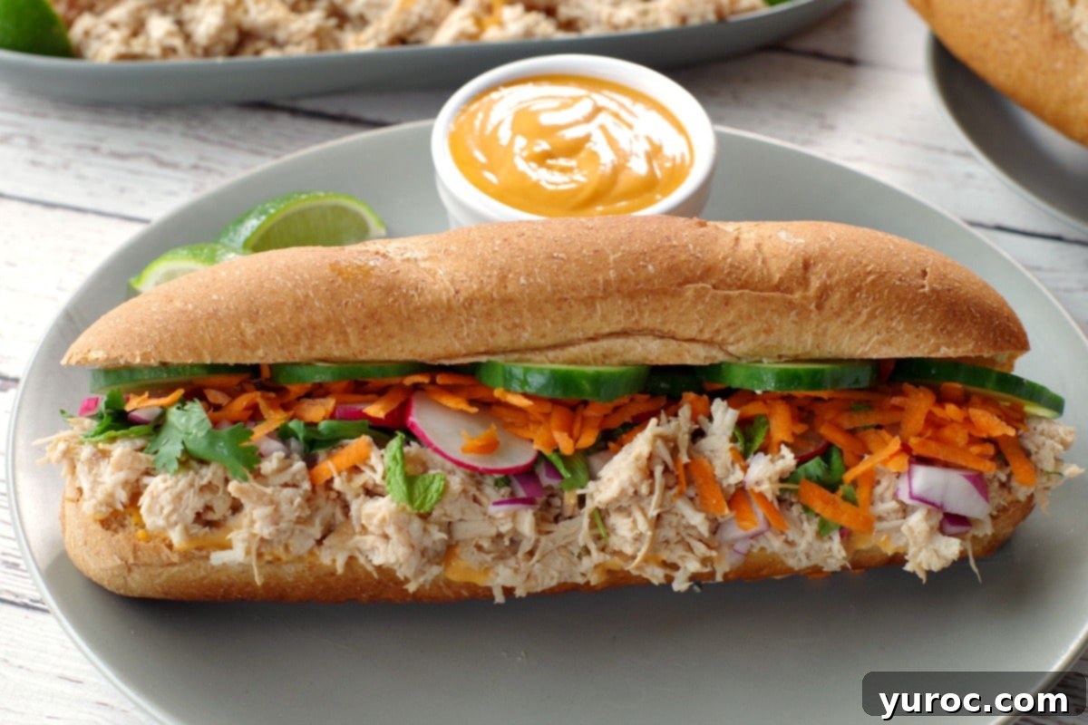 Closed Slow Cooker Chicken Banh Mi Vietnamese Sub on a greenish-grey plate with lime garnish and a small white dish of Sriracha mayonnaise