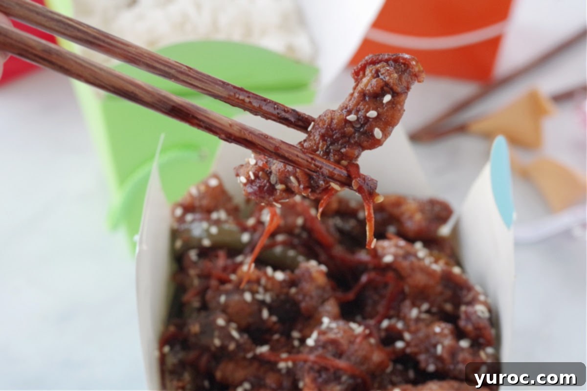 The Ultimate Calgary Ginger Beef 5 a piece of ginger beef being held up with chopsticks over a blue take-out container