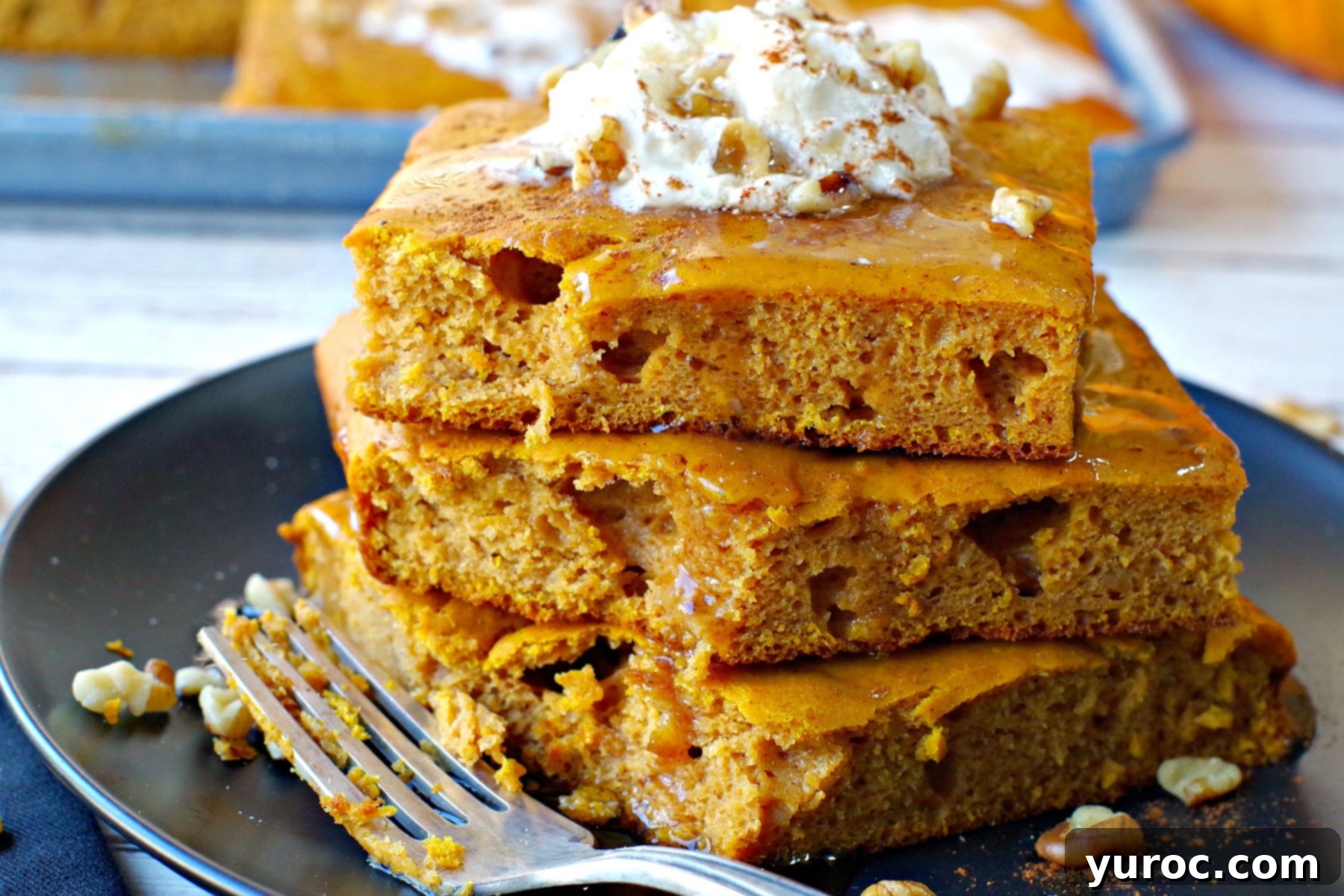 stack of 3 pumpkin pie pancakes on black plate with bite eaten out of stack and fork on the side