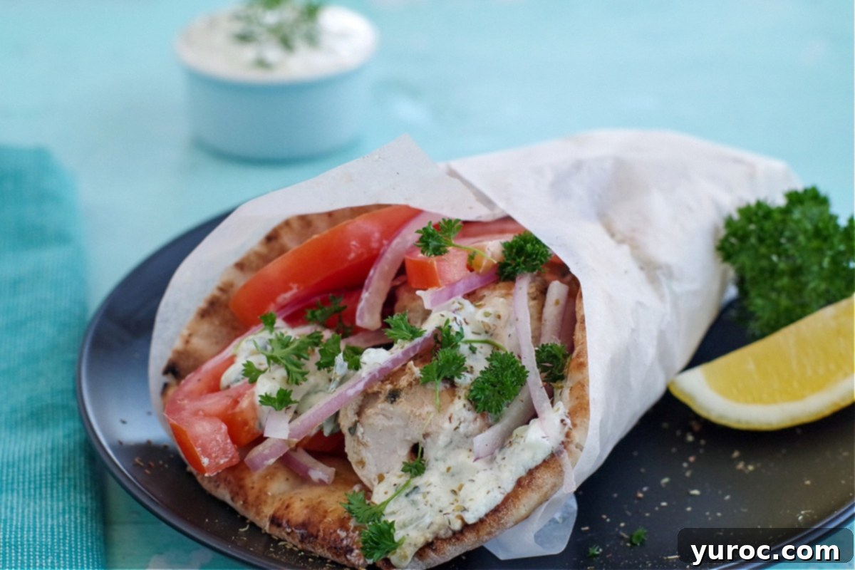Greek chicken souvlaki wrapped in pita with tomatoes, red onion, tzatziki and parsley, wrapped in paper on black plate