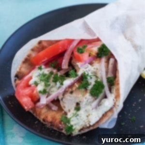 Greek chicken souvlaki wrapped in pita with tomatoes, red onion, tzatziki and parsley, wrapped in paper on black plate